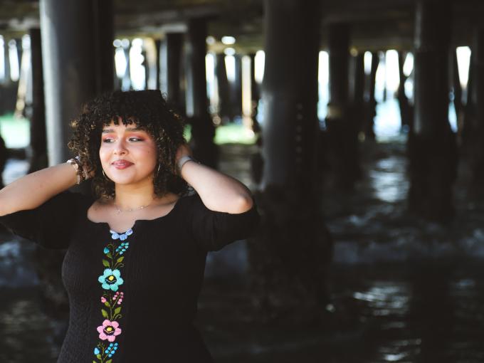 AJ posing and holding her hair under a pier at the beach